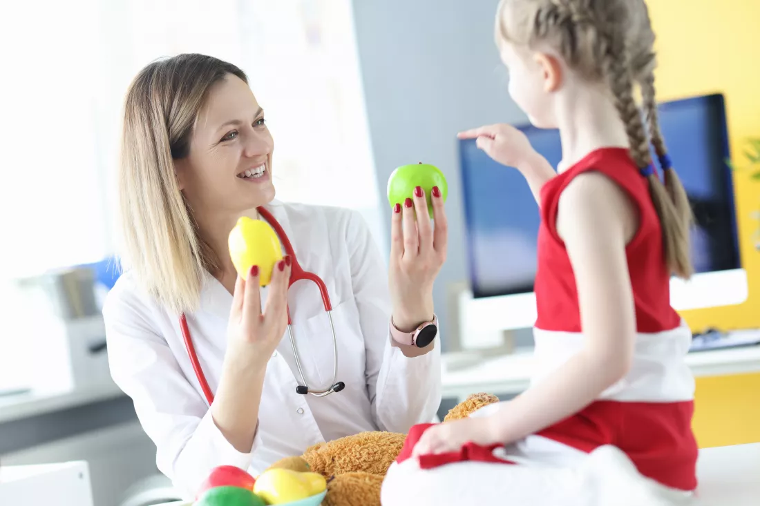 woman-doctor-giving-fruit-little-girl-clinic