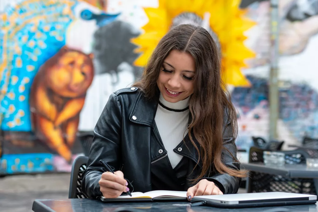 Studentka robi notatki w notesie przy stoliku w kawiarni