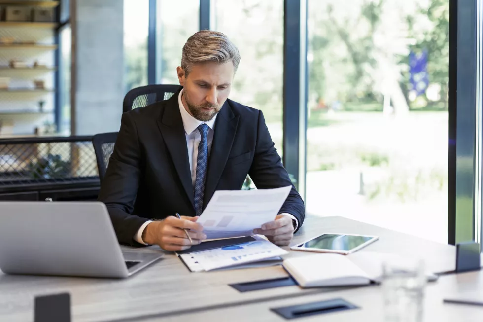 mature-businessman-with-beard-working-with-documents-contracts-bills-sitting-table