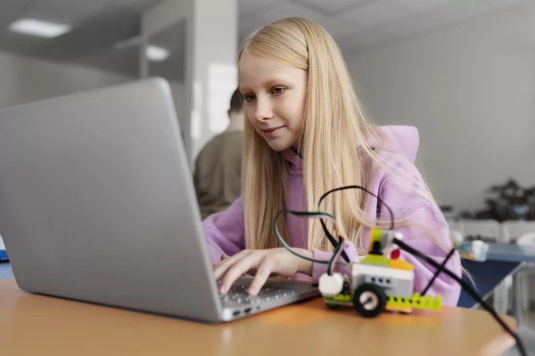 young-girl-using-laptop-electronic-parts-build-robot