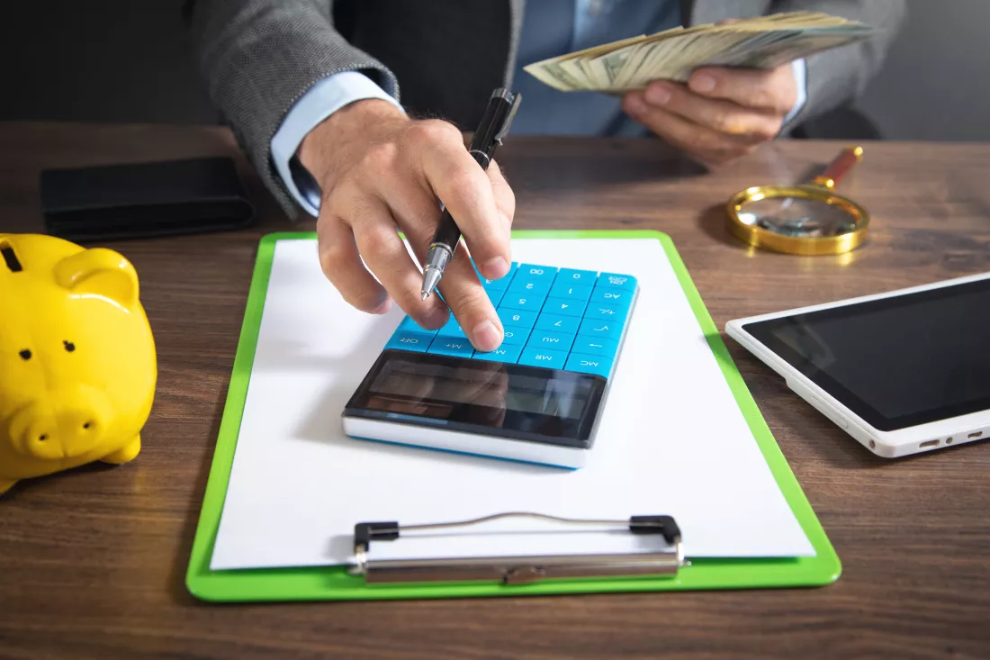 man-using-calculator-holding-dollars