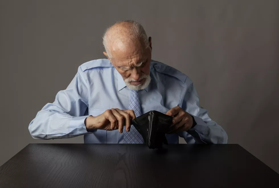 senior-man-checking-wallet-while-sitting-table-against-gray-background