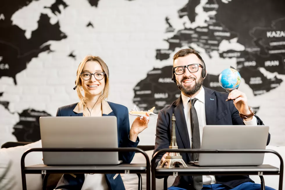 couple-travel-managers-working-online-with-laptops-headsets-agency-office-with-world-map-background
