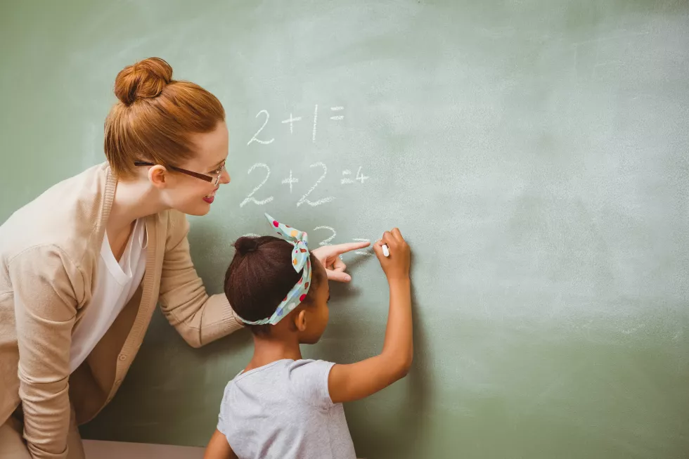 teacher-assisting-girl-write-blackboard-classroom