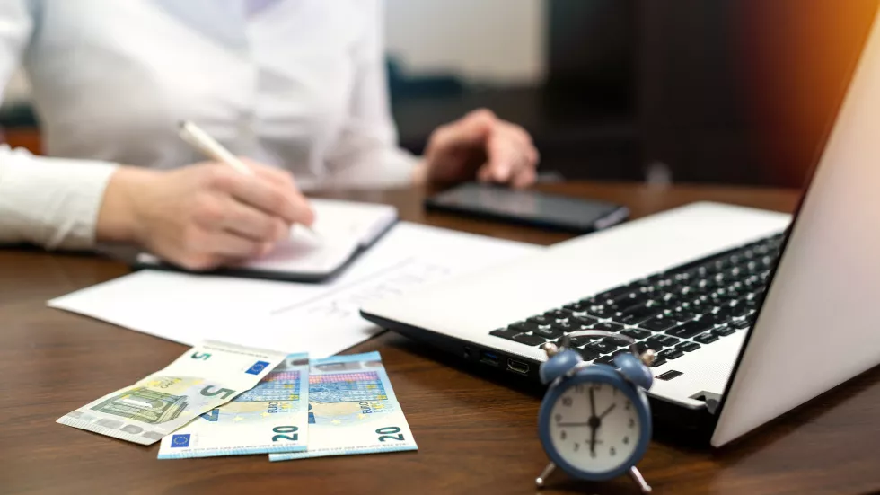 woman-working-with-finances-table-laptop-smartphone-money-notepad-clock