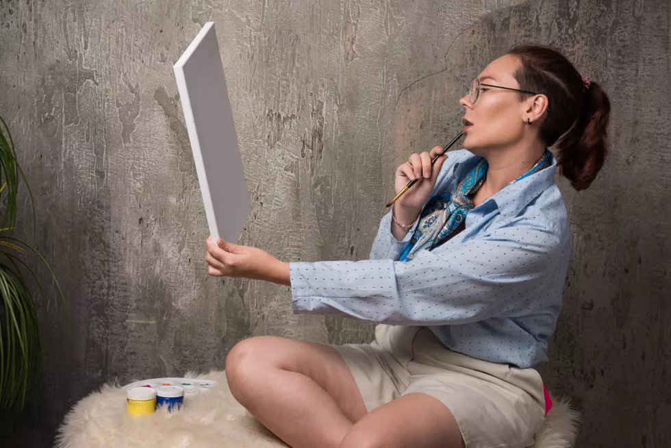 woman-sitting-looking-canvas-with-brush-marble-background