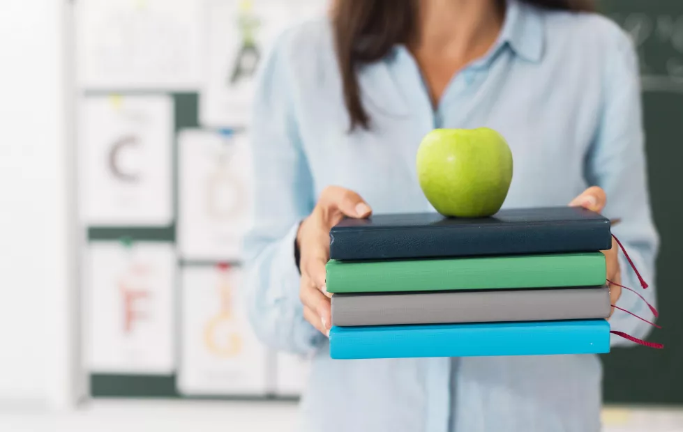 smiley-teacher-holding-bunch-books-apple