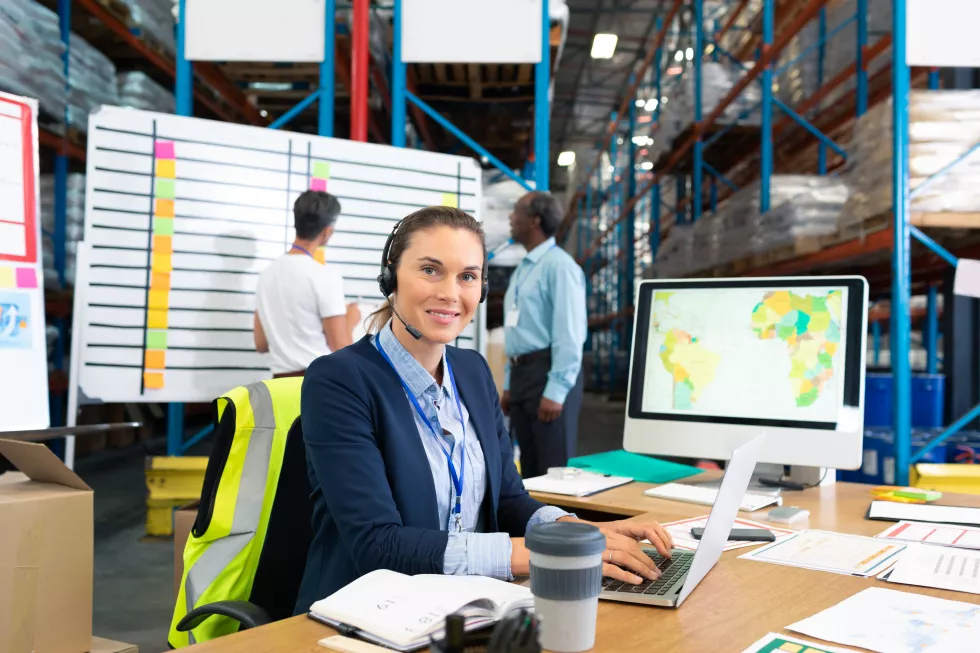 female-manager-with-headset-using-laptop-desk-warehouse