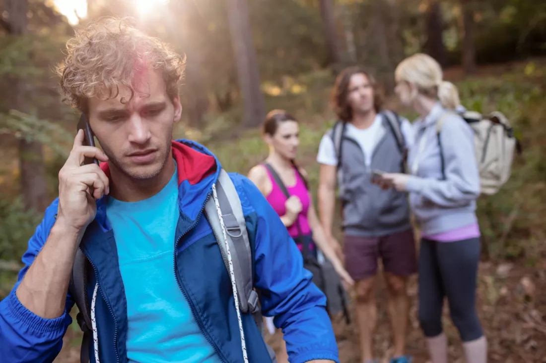 young-man-talking-phone-while-hiking-with-his-friends