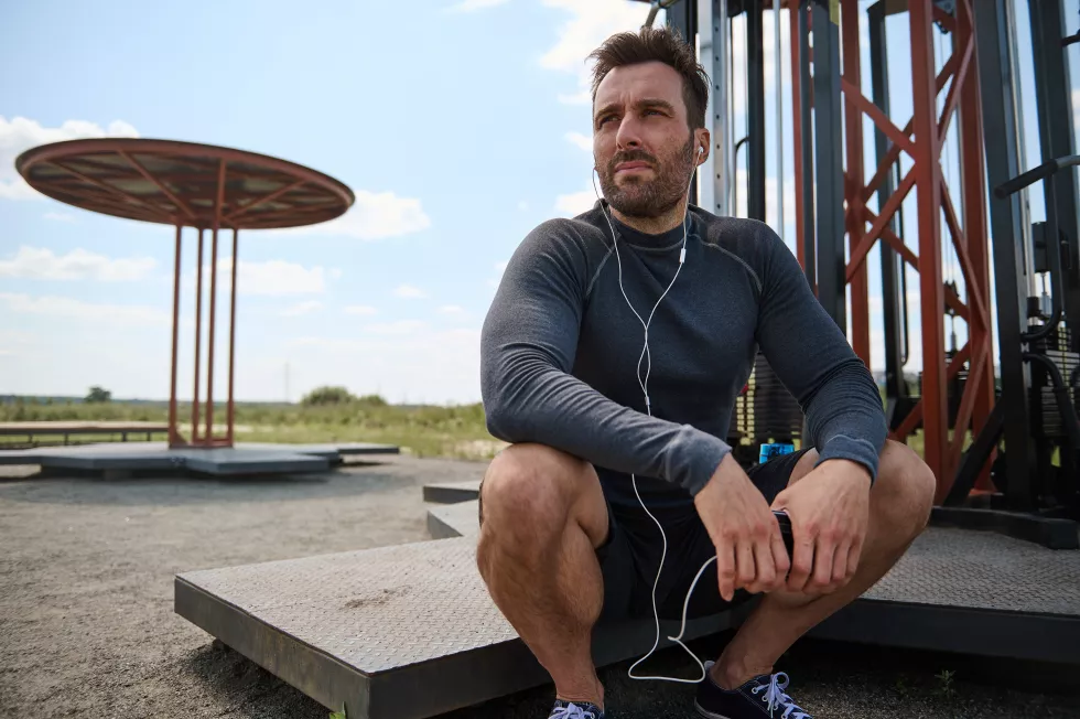close-up-portrait-handsome-caucasian-european-mixed-race-guy-young-sportsman-wearing-earphones-resting-sportsground-after-workout-with-smartphone-hands