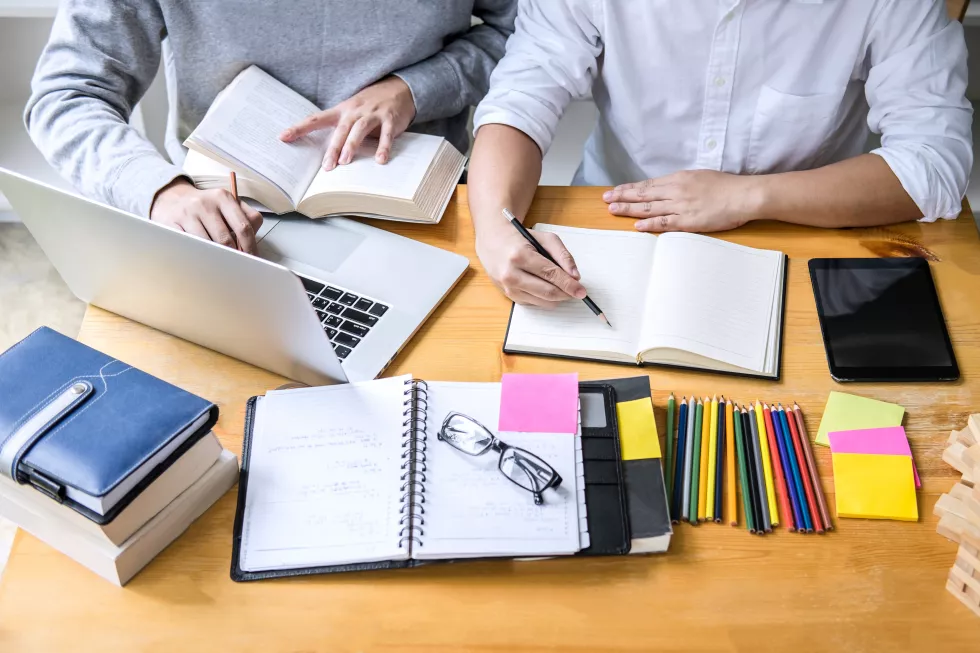 midsection-friends-writing-diary-while-discussing-book-laptop