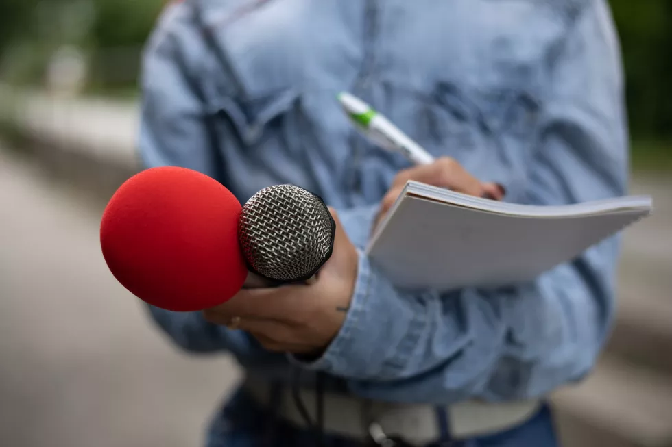 female-journalist-news-conference-writing-notes-holding-microphone
