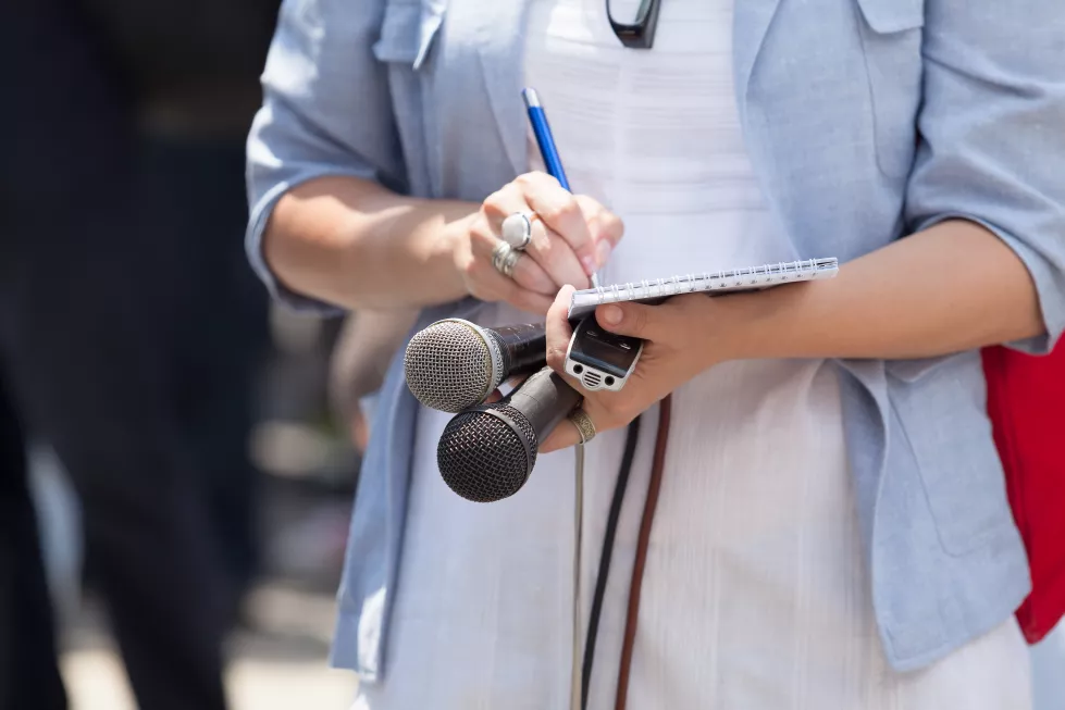 midsection-journalist-holding-microphones-while-writing-note-pad(1)