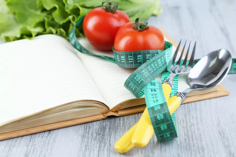 cutlery-tied-with-measuring-tape-book-with-vegetables-wooden-background