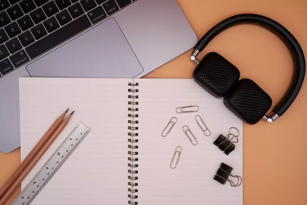 directly-shot-laptop-with-office-supplies-headphones-brown-background