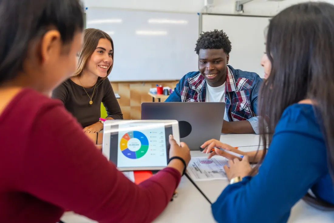 International students discuss charts on a tablet and laptop during a group class