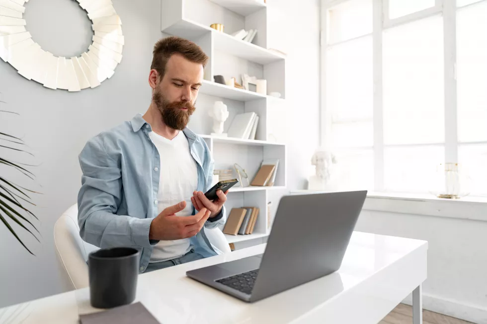 young-bearded-businessman-working-from-home-sitting-desk-talking-mobile-phone
