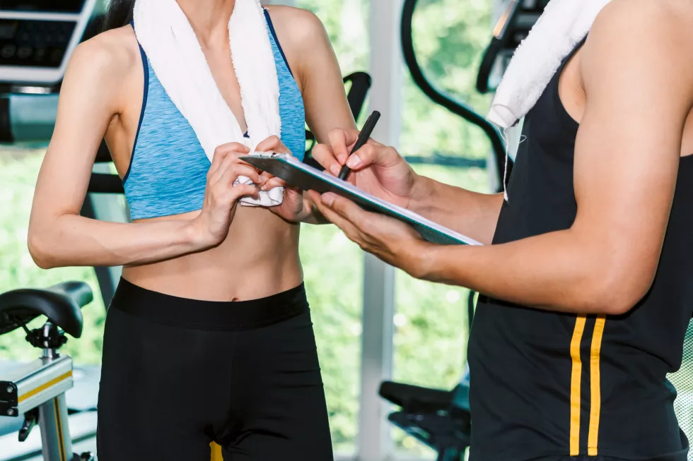 handsome-trainer-fitness-woman-with-towel-stand-gym