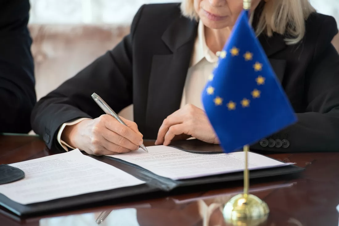 flag-european-union-table-against-mature-female-delegate-signing-contract-after-negotiating-making-deal-by-table-boardroom