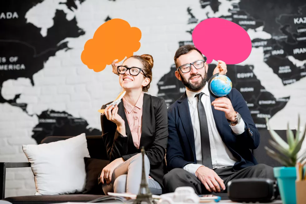 couple-travel-managers-dreaming-with-colorful-bubbles-head-sitting-agency-office-with-world-map-background
