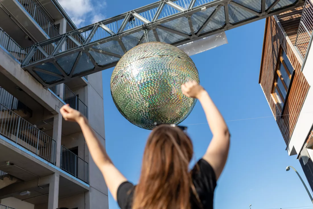low-angle-view-woman-with-arms-raised-against-disco-ball-hanging-from-built-structure