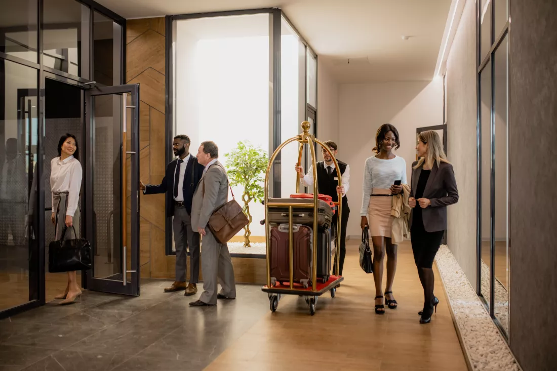 contemporary-business-people-communicating-while-porter-moving-them-pushing-cart-with-baggage-inside-hotel