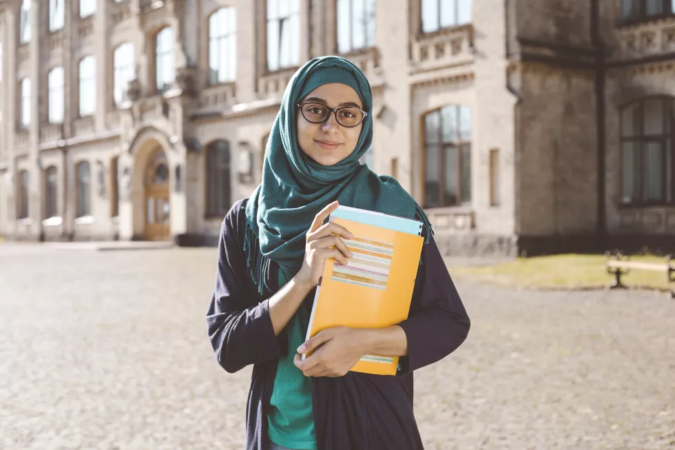 smiling-muslim-young-female-student-holding-books-standing-near-college-happy-arabian-girl-hijab-asian-woman-training
