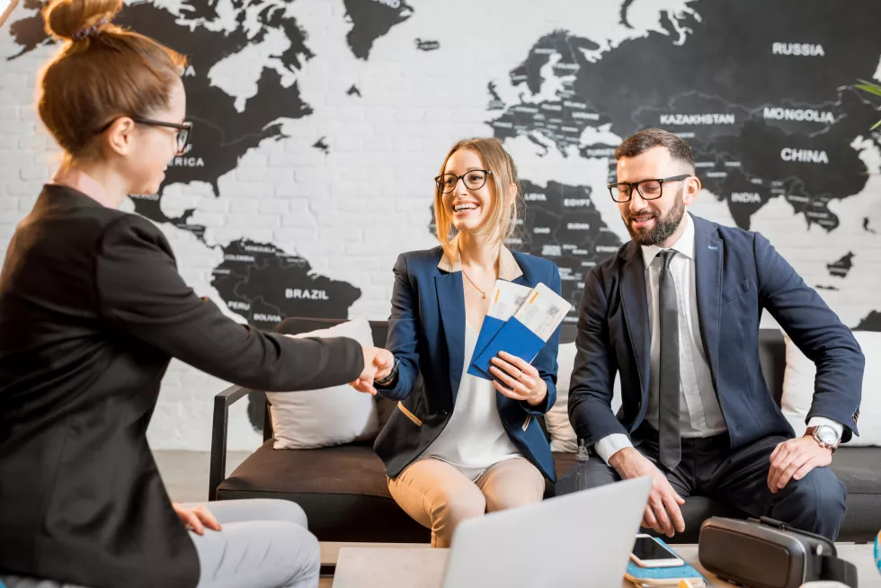 young-businesscouple-choosing-trip-with-agent-sitting-travel-agency-office-with-world-map-background