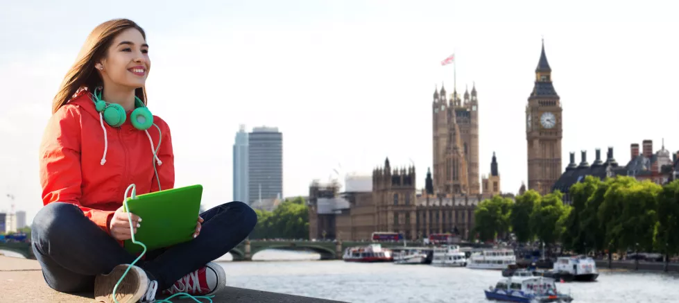 technology-travel-tourism-music-people-concept-smiling-young-woman-teenage-girl-with-tablet-pc-computer-headphones-london-city-big-ben-tower-background