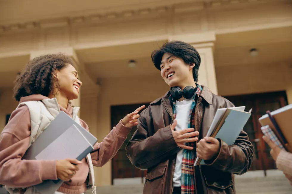 young-students-talking-laughing-together-outdoor-standing-near-campus-holding-books