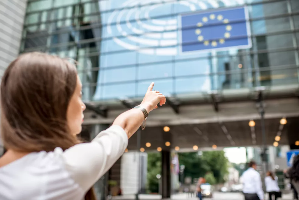 woman-pointing-with-hand-european-flag-parliament-building-brussel