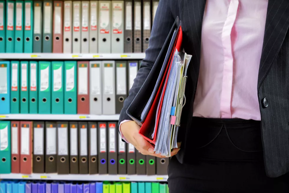 businesswoman-holding-data-files-binder-shelves-background
