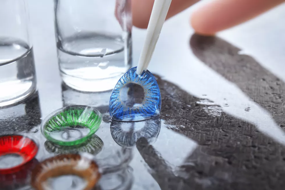 woman-holding-tweezers-with-contact-lens-gray-table
