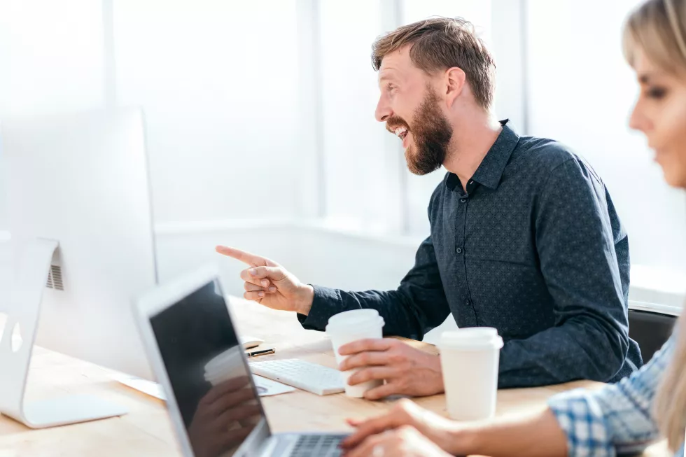 smiling-businessman-talking-colleague-sitting-his-desk