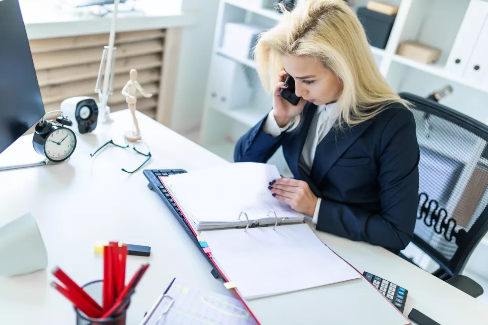 young-woman-sitting-desk-office-talking-phone-looking-documents