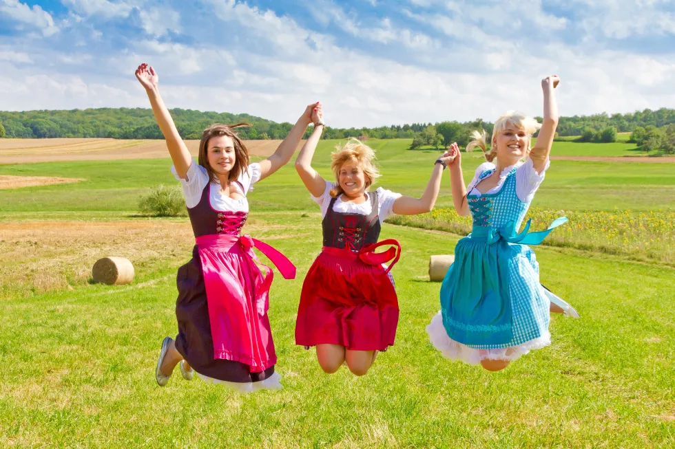 smiling-female-friends-with-dirndl-jumping-field-against-sky