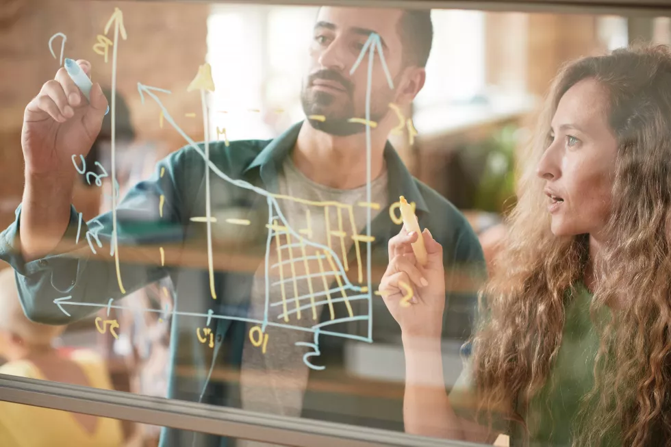 business-colleagues-drawing-financial-graphic-glass-wall-examining-it-together-team-presentation-office(1)