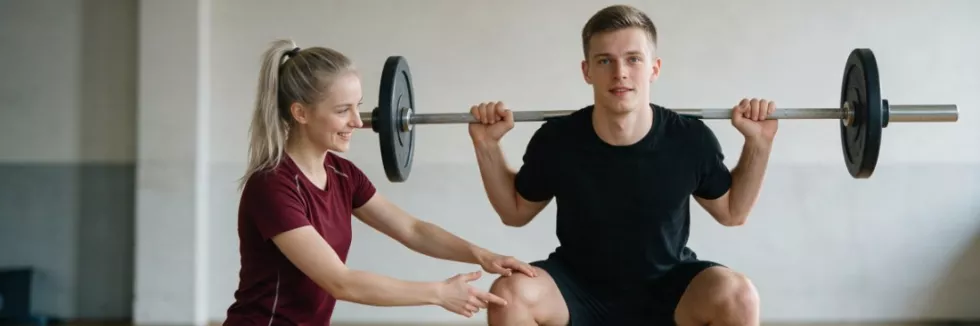 studentka-trenerka-koryguje-technike-przysiadu-na-silowni