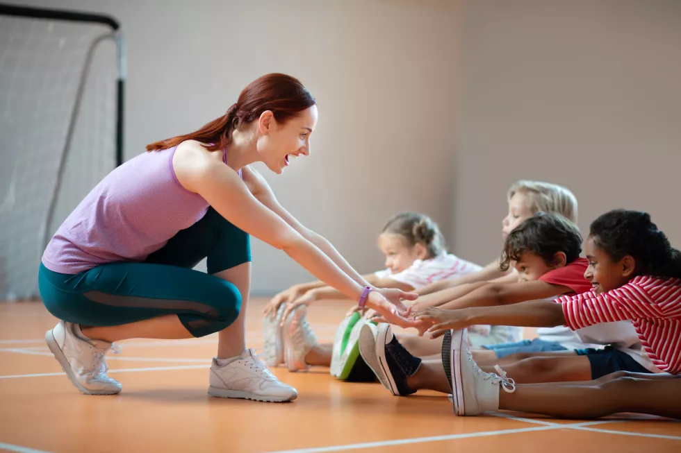 pe-teacher-wearing-leggings-smiling-while-helping-girl-stretching