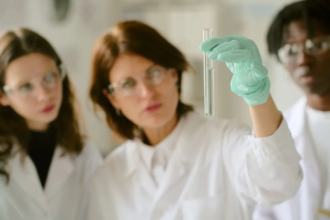 A team of young scientists in lab coats and safety glasses examines a test tube in a chemistry lab